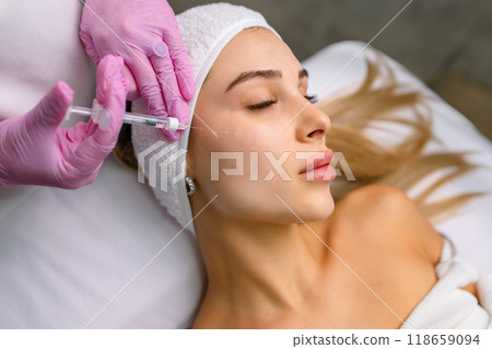 Beautiful relaxed woman at beautician cabinet receiving anti wrinkle injections on cheekbones, lying with closed eyes in beauty salon 118659094