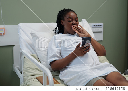 Pregnant Woman Relaxing in Hospital Bed and Browsing Phone 118659158