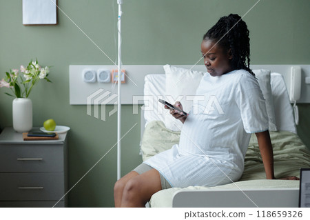 Pregnant Woman Sitting in Hospital Bed Checking Smartphone 118659326