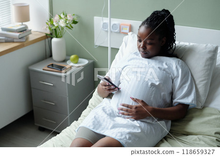 African American Woman Sitting in Hospital Bed Holding Phone 118659327