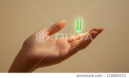 A hand hovers beneath a glowing green pill floating in mid-air 118660522