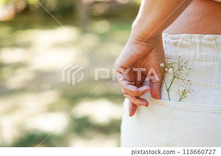 female hand on the back pocket of white pants, with a small spri 118660727