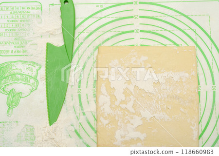 Green knife and floured dough on a silicone kitchen mat. Green knife and floured dough on a silicone kitchen mat. 118660983