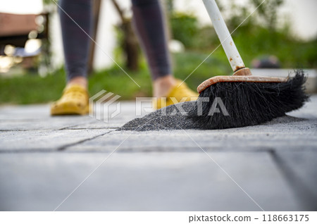 Person brushing filling sand into the gaps between newly layed concrete tiles in a do it yourself project 118663175