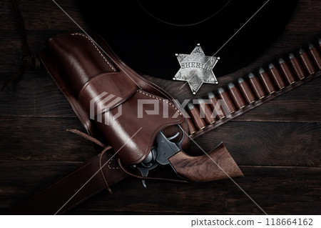 Old west sheriff star badge with gun, holster and gun belt with old west hat on table. Top view. Old west sheriff star badge with gun, holster and gun belt with old west hat on table. Top view. 118664162