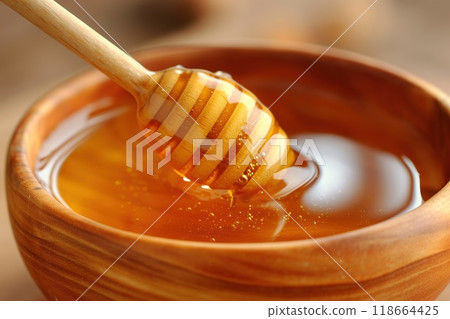 Honey dripping from a wooden honey dipper into a wooden bowl 118664425