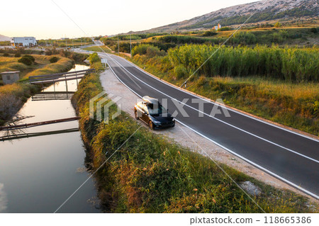 A black vehicle equipped with a roof rack is parked along a serene road, surrounded by greenery A black vehicle equipped with a roof rack is parked along a serene road, surrounded by greenery 118665386