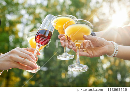 Four hands holding various drinks including champagne and juice under sunlight Creating a cheerful and festive atmosphere with nature backdrop Four hands holding various drinks including champagne and juice under sunlight Creating a cheerful and festive atmosphere with nature backdrop 118665516