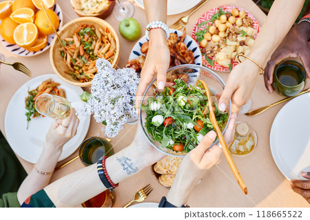 Table filled with variety of Mediterranean dishes being served, showing hands with plates and drinks capturing the vibrant communal meal setting, group gathering during daylight Table filled with variety of Mediterranean dishes being served, showing hands with plates and drinks capturing the vibrant communal meal setting, group gathering during daylight 118665522
