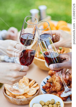 Close-up of hands raising wine glasses during picnic including snacks, olives, and crackers on table. Cheers and camaraderie in outdoor setting with diverse participants Close-up of hands raising wine glasses during picnic including snacks, olives, and crackers on table. Cheers and camaraderie in outdoor setting with diverse participants 118665526