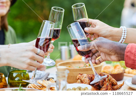Group of people celebrating at outdoor dinner party with various foods on table while clinking glasses of red wine creating joyful and festive atmosphere Group of people celebrating at outdoor dinner party with various foods on table while clinking glasses of red wine creating joyful and festive atmosphere 118665527