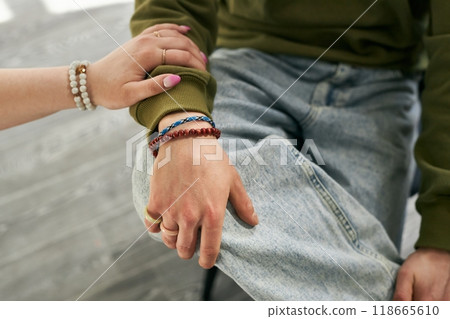 Close-up of two individuals' hands, showing bracelets and casual arm placement. The jeans and green sweater create a relaxed atmosphere Close-up of two individuals' hands, showing bracelets and casual arm placement. The jeans and green sweater create a relaxed atmosphere 118665610
