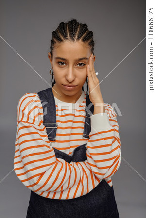 Vertical waist up portrait of smug young woman with cornrows hairstyle posing confidently on grey background in studio and looking at camera Vertical waist up portrait of smug young woman with cornrows hairstyle posing confidently on grey background in studio and looking at camera 118666175