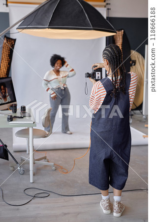 Full length back view of young woman as female photographer taking pictures of model in professional photo studio Full length back view of young woman as female photographer taking pictures of model in professional photo studio 118666188