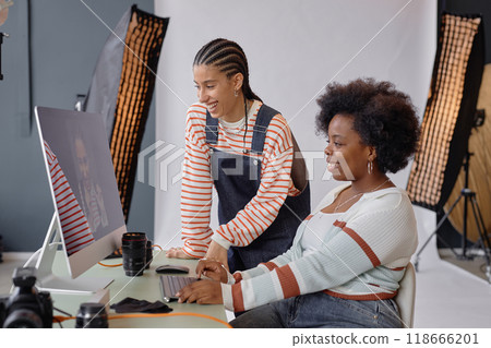 Side view portrait of two smiling young women looking at pictures on computer screen during professional photoshoot in studio Side view portrait of two smiling young women looking at pictures on computer screen during professional photoshoot in studio 118666201