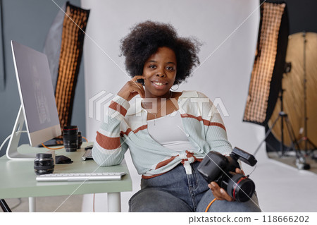 Portrait of smiling African American woman as photographer looking at camera at workplace in photo studio and holding camera, copy space Portrait of smiling African American woman as photographer looking at camera at workplace in photo studio and holding camera, copy space 118666202