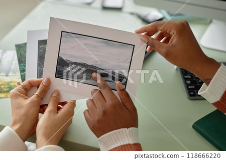 Close up of two women holding photo prints with nature landscapes and discussing images for creative project copy space 118666220