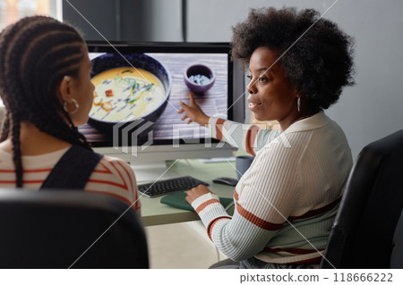Side view portrait of creative young Black woman discussion photos with friend or colleague and pointing at computer screen Side view portrait of creative young Black woman discussion photos with friend or colleague and pointing at computer screen 118666222