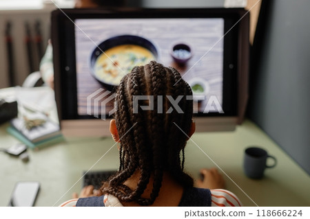 Back view of young Black woman with cornrows hairstyle editing pictures using professional PC in studio 118666224