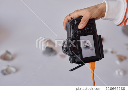 Closeup of female hand holding pro DSLR camera and taking product pictures in minimal studio set copy space 118666288