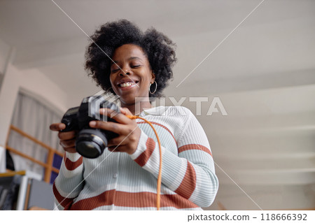 Candid low angle portrait of smiling Black woman as female photographer holding camera and looking at pictures on screen copy space 118666392