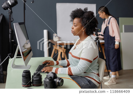 Side view portrait of Black female photographer using computer for edit and retouch in professional photo studio copy space Side view portrait of Black female photographer using computer for edit and retouch in professional photo studio copy space 118666409