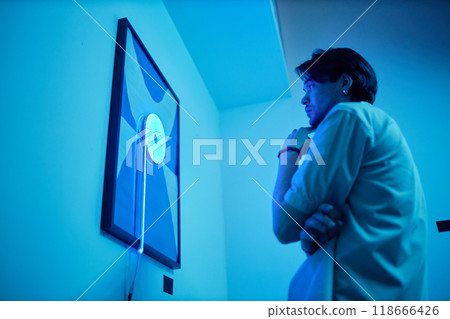 Side view portrait of pensive adult man looking at paintings in blue neon light during modern art show, copy space 118666426