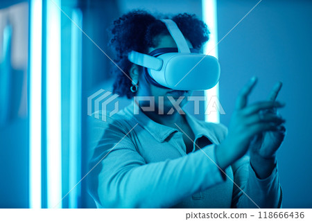 Portrait of African American woman wearing VR headset in modern art show with blue neon lights and reaching out experiencing digital cyberspace 118666436