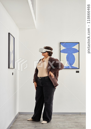 Side view full length portrait of Black adult woman wearing VR headset while looking at paintings in mixed reality modern art exhibition, copy space 118666466