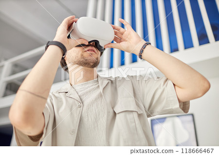Low angle portrait of man wearing VR headset in modern art museum and looking at digital artwork, copy space 118666467