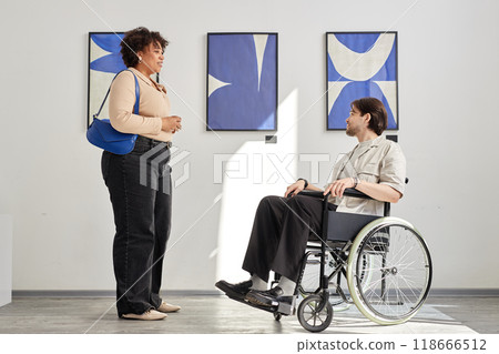 Minimal side view shot of man with disability using wheelchair and talking to friend while visiting accessible art gallery exhibition Minimal side view shot of man with disability using wheelchair and talking to friend while visiting accessible art gallery exhibition 118666512
