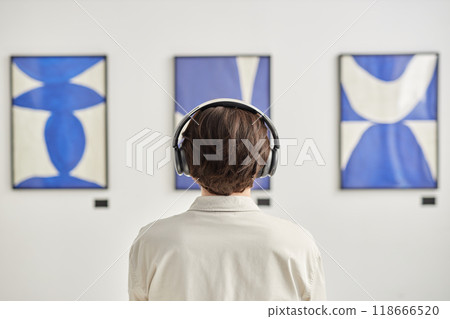 Minimal back view of unrecognizable man wearing headphones looking at abstract paintings in modern art gallery and listening to audio guide copy space Minimal back view of unrecognizable man wearing headphones looking at abstract paintings in modern art gallery and listening to audio guide copy space 118666520
