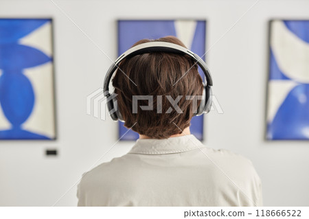 Minimal back view of man wearing headphones looking at abstract paintings visiting modern art gallery show with multisensory experience copy space Minimal back view of man wearing headphones looking at abstract paintings visiting modern art gallery show with multisensory experience copy space 118666522