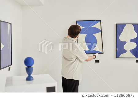 Minimal back view of man hanging abstract art painting on wall while preparing for exhibition in museum copy space 118666672