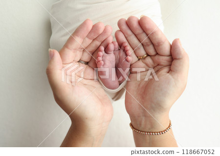 The palms of the parents. A father and mother hold the feet of a newborn child in a white blanket on a white background.. The feet of a newborn in the hands of parents. Photo of foot, heels and toes The palms of the parents. A father and mother hold the feet of a newborn child in a white blanket on a white background.. The feet of a newborn in the hands of parents. Photo of foot, heels and toes 118667052