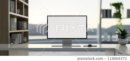 A computer on a white desk in a modern office, featuring a large window with a nature view. 118668372