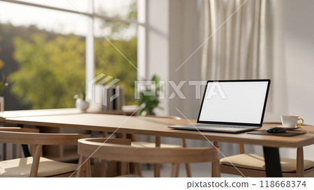 A close-up of a laptop with a white screen mockup on a wooden dining table in a contemporary home. 118668374