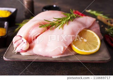 Raw chicken breast or fillet with salt, pepper and fresh herbs on a plate on dark background. Healthy food. Top view, copy space Raw chicken breast or fillet with salt, pepper and fresh herbs on a plate on dark background. Healthy food. Top view, copy space 118669717