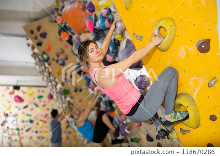 Young female alpinist practicing indoor rock-climbing on a artificial boulder without safety belts 118670286