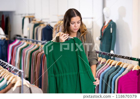Young woman studying the fabrics of modern green sleeveless cardigan in a clothing store 118670379