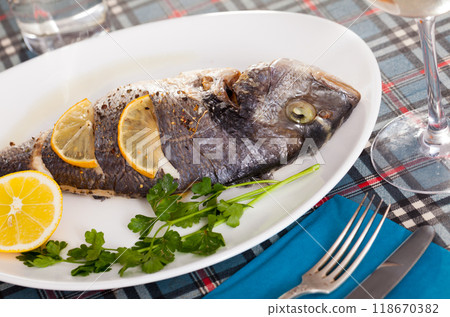 Top view of whole dorada baked with lemon served at plate with greens 118670382