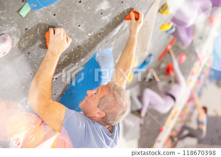 Alpinist practicing indoor rock climbing on artificial boulder without safety belts Alpinist practicing indoor rock climbing on artificial boulder without safety belts 118670398