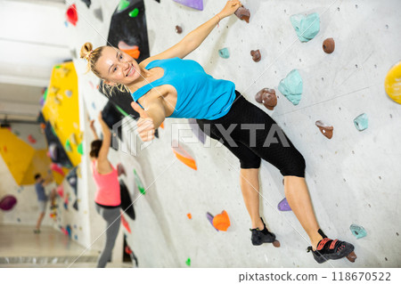 Woman showing thumb up while exercising on artificial climbing wall 118670522
