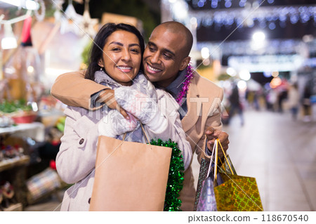 Cheerful couple with bags of gifts walking on christmas fair Cheerful couple with bags of gifts walking on christmas fair 118670540
