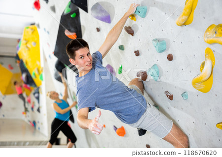 Man showing thumb up while exercising on artificial climbing wall 118670620