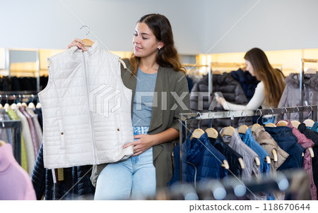 Young lady in casual clothes with white autumn gilet in the middle of the clothing store Young lady in casual clothes with white autumn gilet in the middle of the clothing store 118670644