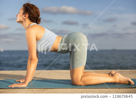 Yoga practice on embankment, female athlete fulfil carry out Marjariasana Yoga practice on embankment, female athlete fulfil carry out Marjariasana 118670645