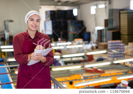 Positive female worker fills out a document at a citrus processing plant. Positive female worker fills out a document at a citrus processing plant. 118670666