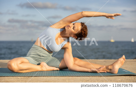 Yoga practice on embankment, female athlete fulfil carry out Janu Shirshasana 118670676