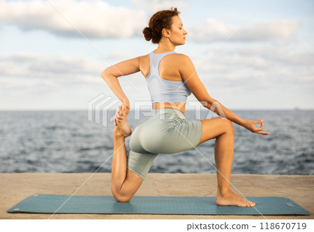 Yoga practice on embankment, female athlete fulfil carry out Anjaneyasana Yoga practice on embankment, female athlete fulfil carry out Anjaneyasana 118670719